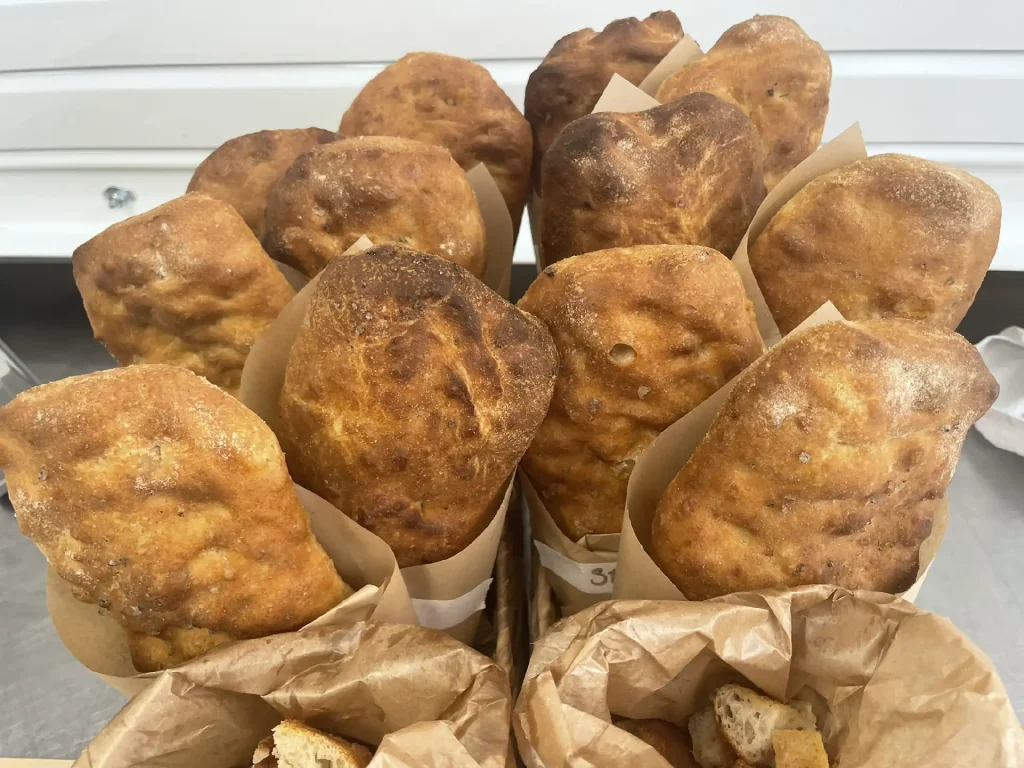 Pile of crusty brown dinner rolls nestled in parchment paper liners more rolls rise behind them in a basket like arrangement