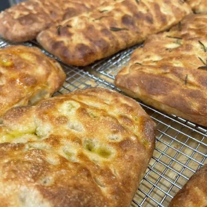 Golden brown marvelli focaccia bread loaves with rosemary sprinkled on top cooling on a wire rack