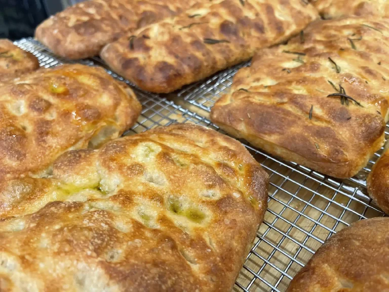 Golden brown marvello focaccia loaves with rosemary sprinkled on top cooling on a wire rack