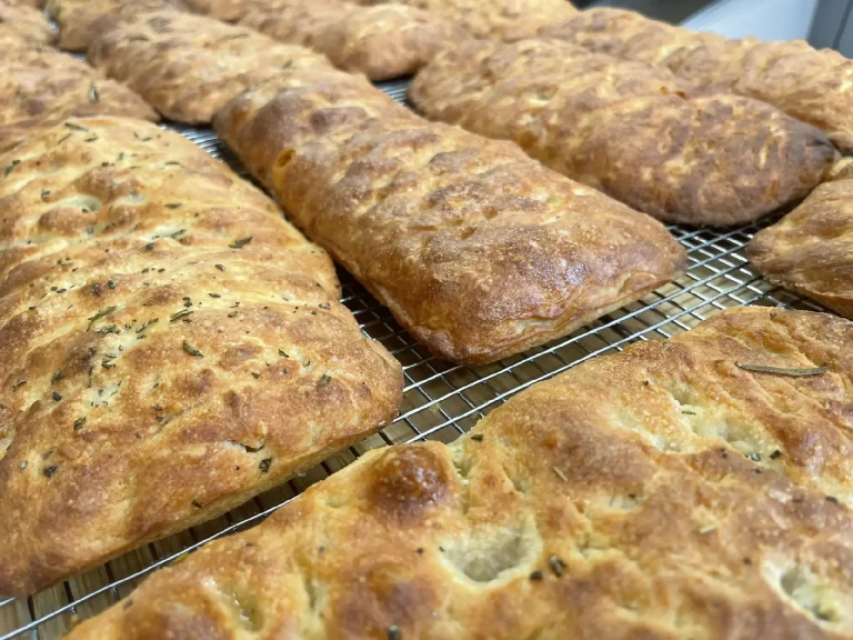 Golden brown crusty loaves cooling on a wire rack speckled with herb flecks