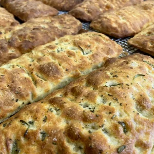Golden brown marvelli focaccia loaves cooling on a rack studded with rosemary