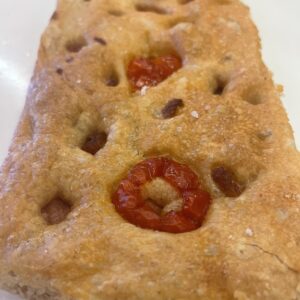 Golden brown marvelli focaccia topped with roasted cherry tomatoes and coarse salt flakes on a pale plate
