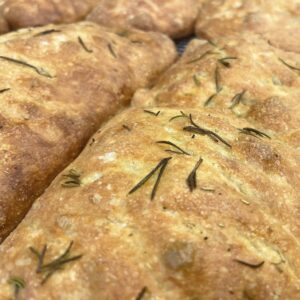 Close up of golden brown marvelli focaccia bread studded with rosemary sprigs on a cooling rack