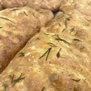 Marvelli Focaccia Bread Studded with Rosemary | Marvelli Artisan Breads Close up of golden brown marvelli focaccia bread studded with rosemary sprigs on a cooling rack