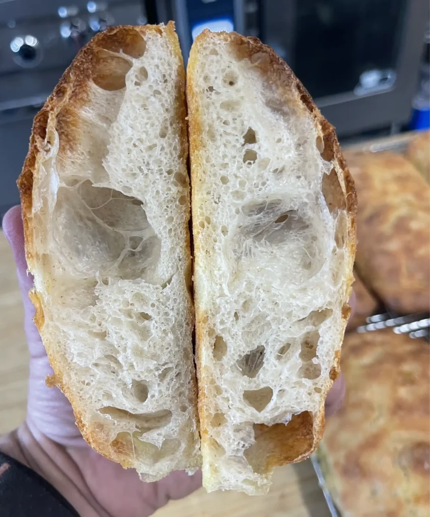 Two halves of a crusty baguette held apart revealing an airy hole filled crumb and golden crust