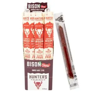 Bison Chipotle Meat Sticks | Marvelli Artisan Breads Chipotle flavored bison meat sticks in red and white packaging stacked with extra wrapper to the side on white background